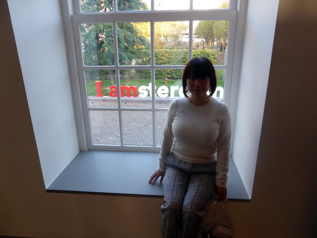 Miaomiao at a window at the Ground Floor of the Hermitage Amsterdam museum, with a view on the `I Amsterdam` sign at the Hoftuin garden