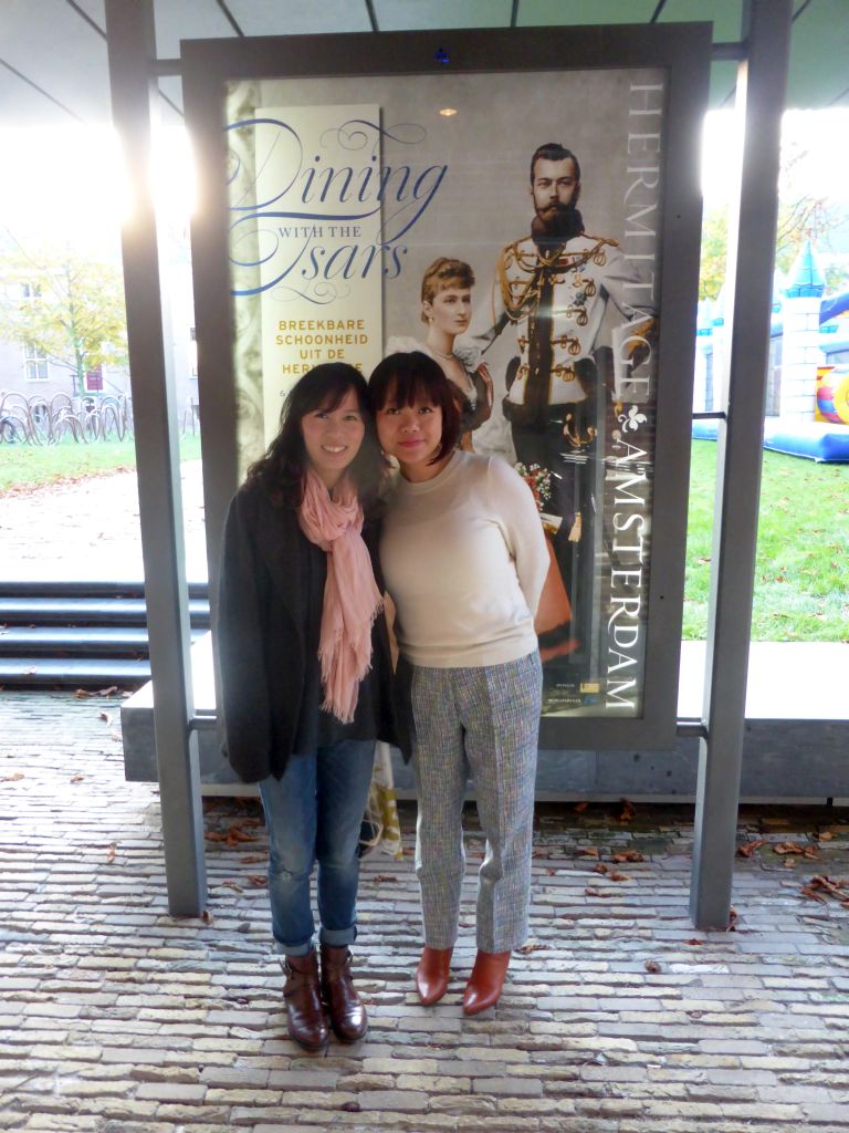Miaomiao and Mengjin in front of a poster on the exhibition `Dining with the Tsars` at the back side of the Hermitage Amsterdam museum
