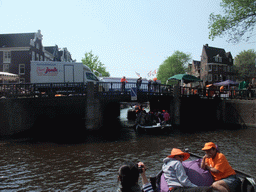 Jola and Irene on the tour boat at the Prinsengracht canal, with the bridge at the crossing of the Westermarkt square, and people with wooden shoes on a fishing pole