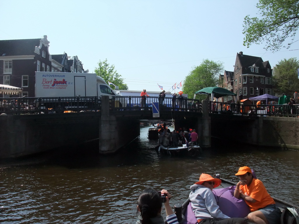 Jola and Irene on the tour boat at the Prinsengracht canal, with the bridge at the crossing of the Westermarkt square, and people with wooden shoes on a fishing pole