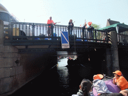 Jola and Irene on the tour boat at the Prinsengracht canal, with the bridge at the crossing of the Westermarkt square, and people with wooden shoes on a fishing pole