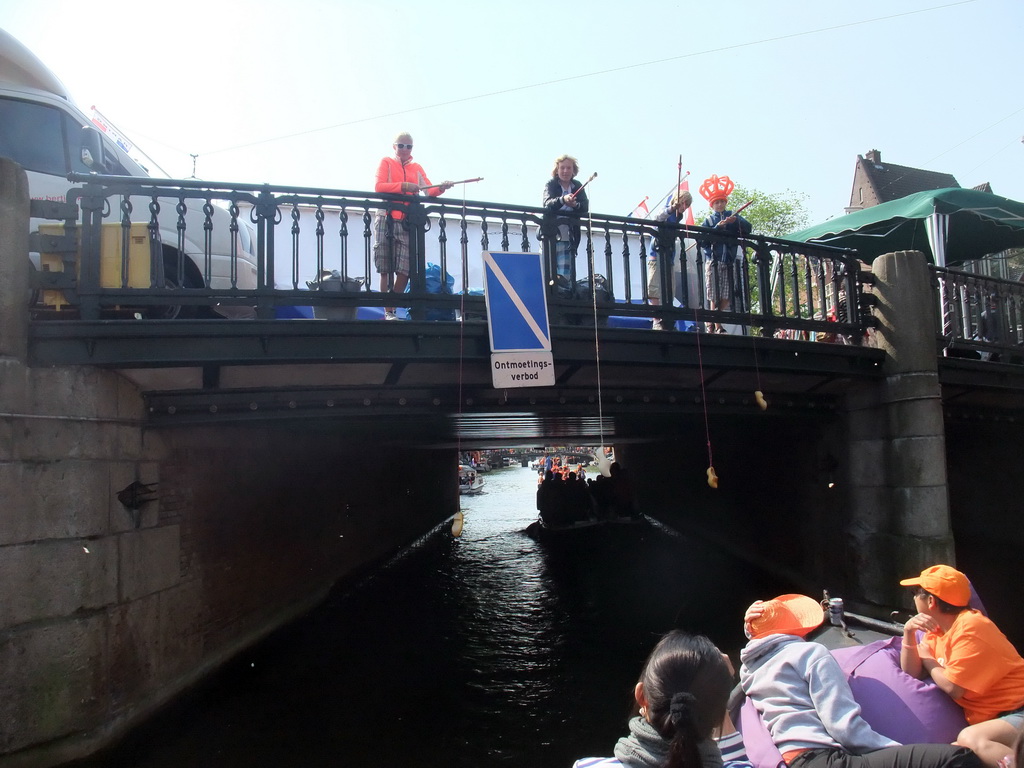 Jola and Irene on the tour boat at the Prinsengracht canal, with the bridge at the crossing of the Westermarkt square, and people with wooden shoes on a fishing pole