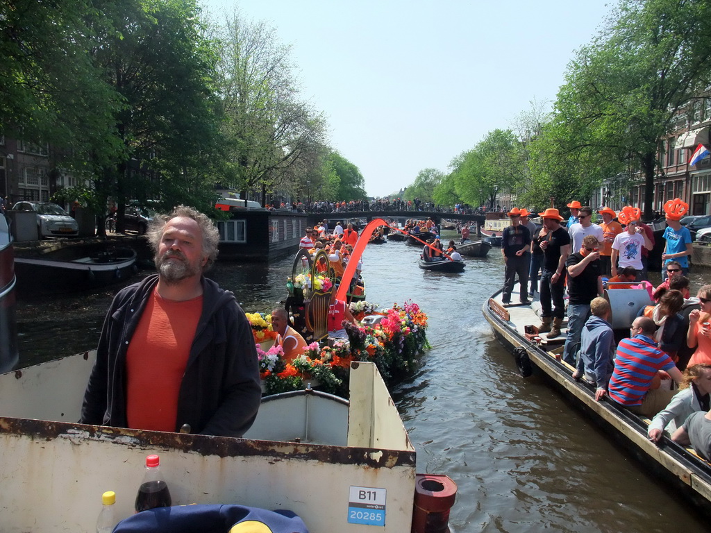 The skipper on the tour boat at the Singel canal with a flower boat and the bridge at the crossing of the Korte Korsjespoortsteeg street