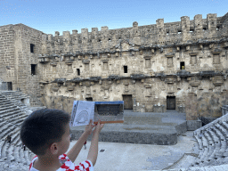 Max with a reconstruction in a travel guide at the diazoma of the west auditorium of the Roman Theatre of Aspendos, with a view on the orchestra, stage and stage building