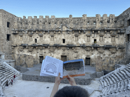 Max with a reconstruction in a travel guide at the diazoma of the west auditorium of the Roman Theatre of Aspendos, with a view on the orchestra, stage and stage building