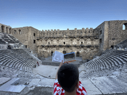Max with a reconstruction in a travel guide at the diazoma of the west auditorium of the Roman Theatre of Aspendos, with a view on the orchestra, stage and stage building