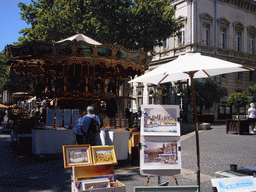 Carousel, drawings and street shops at the Place de l`Horloge square