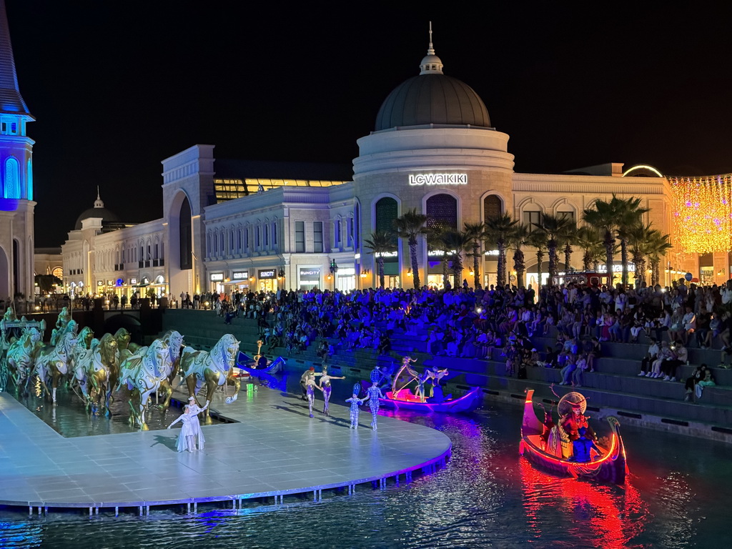 Boats, actors and horse statues in front of the Chateau at the Shopping Avenue area of the Land of Legends theme park, during the Musical Boat Parade, by night