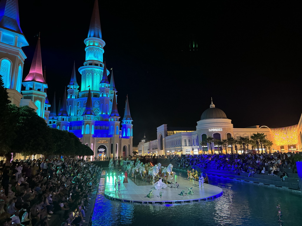 Boats, actors and horse statues in front of the Chateau at the Shopping Avenue area of the Land of Legends theme park, during the Musical Boat Parade, by night