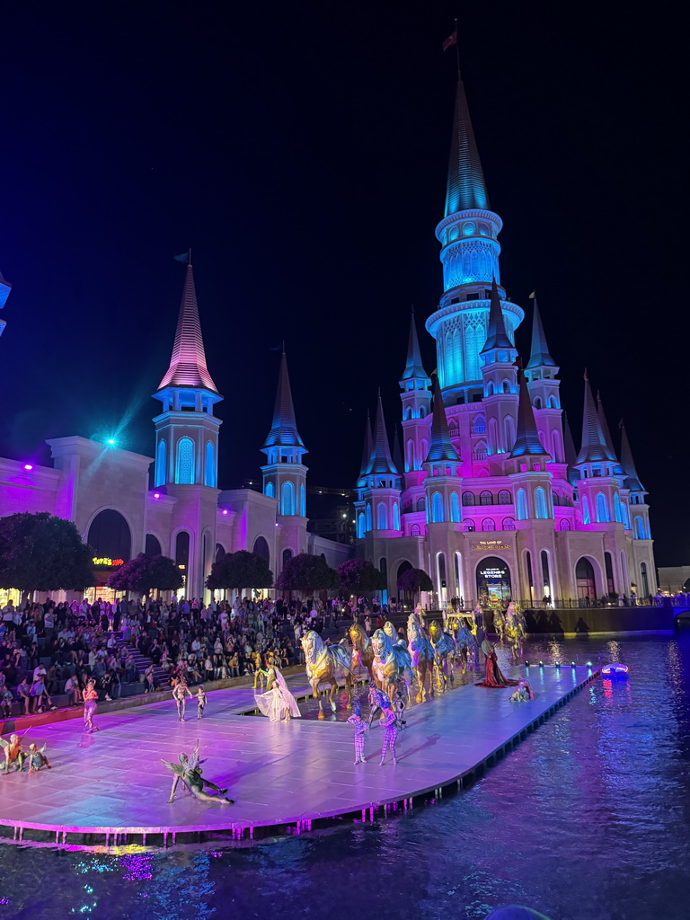 Boats, actors and horse statues in front of the Chateau at the Shopping Avenue area of the Land of Legends theme park, during the Musical Boat Parade, by night