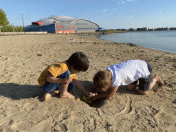 Max and his friend playing with toys and sand at the beach at the Binnenschelde lake, with a view on the Schelp swimming pool