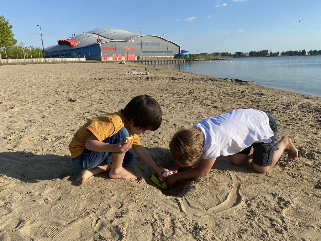 Max and his friend playing with toys and sand at the beach at the Binnenschelde lake, with a view on the Schelp swimming pool