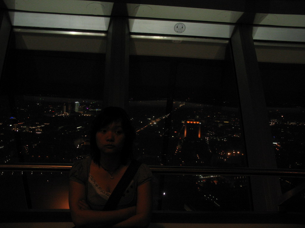 Miaomiao at the viewing point on top of the Fernsehturm tower, with a view on the west side of the city, by night