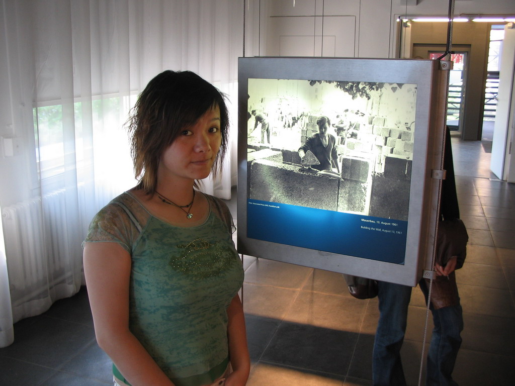 Miaomiao with a photograph of someone building the Berlin Wall, at the Gedenkstätte Berliner Mauer museum