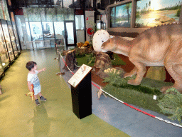 Max with a dinosaur toy and statues of Triceratopses, a dinosaur egg, Maiasaura eggs and a Maiasaura at the Lower Floor of the Museum Building of the Oertijdmuseum