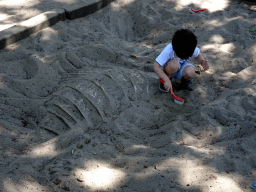 Max with a brush at the dinosaur excavation sandbox at the Oertijdwoud forest of the Oertijdmuseum