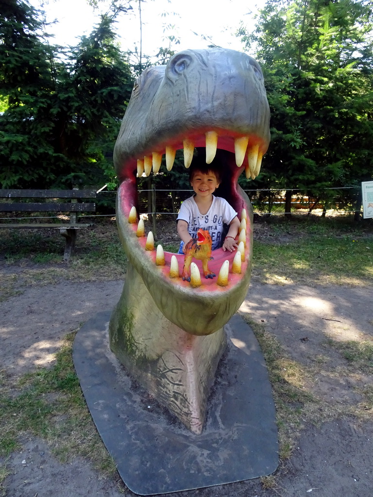Max with a dinosaur toy in a statue of the head of a Dinosaur at the playground in the Oertijdwoud forest of the Oertijdmuseum