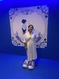 Miaomiao with wooden shoes in front of a Delfts Blauw painted tile at the SuperNova Experience museum