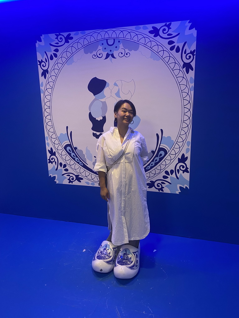 Miaomiao with wooden shoes in front of a Delfts Blauw painted tile at the SuperNova Experience museum