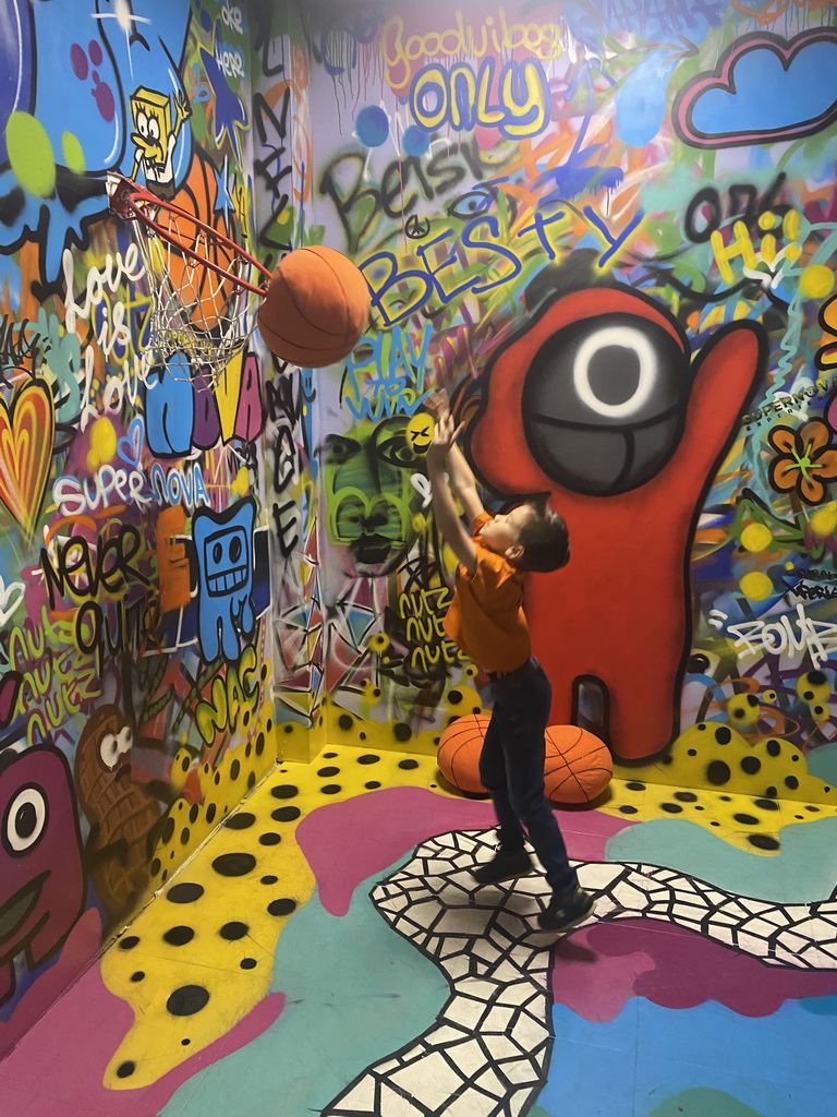 Max throwing a basketball at the graffiti room at the SuperNova Experience museum