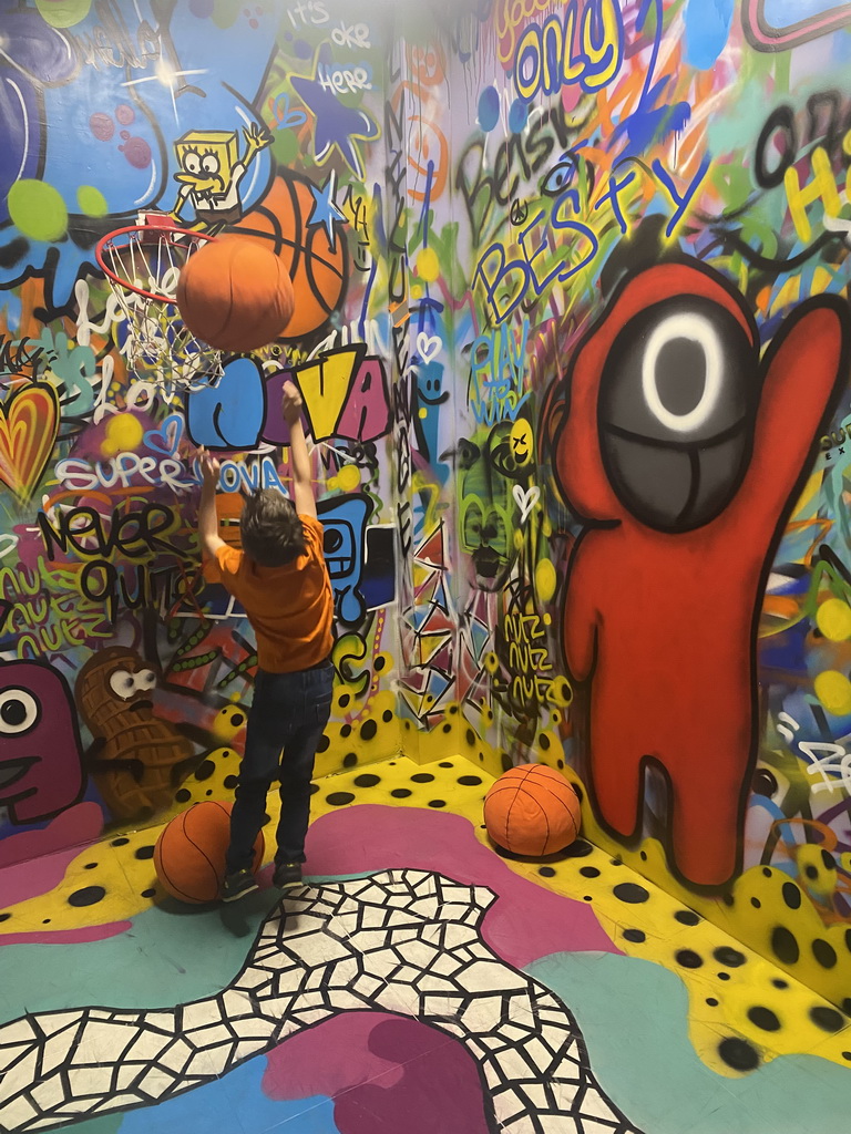 Max throwing a basketball at the graffiti room at the SuperNova Experience museum