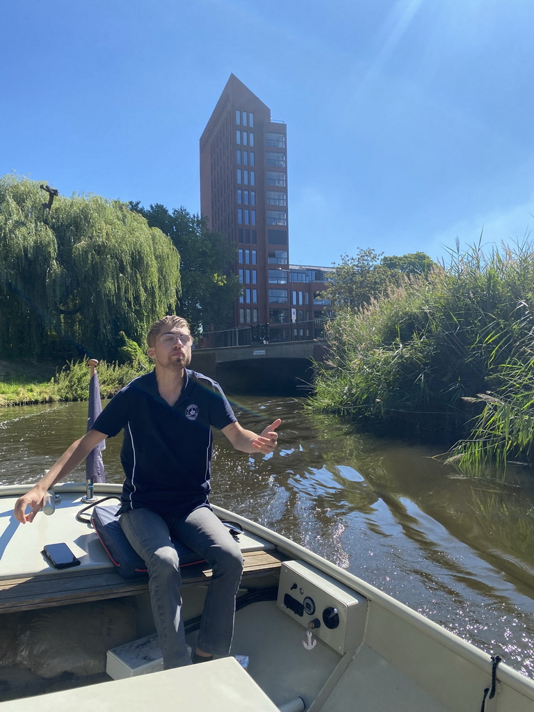 Tour guide on our tour boat on the Aa of Weerijs river, with a view on the Irenebrug bridge and a building at the Marksingel street