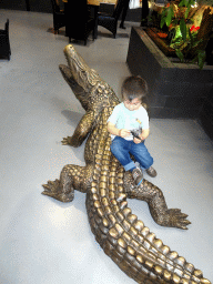 Max sitting on a crocodile statue at the lower floor of the Reptielenhuis De Aarde zoo