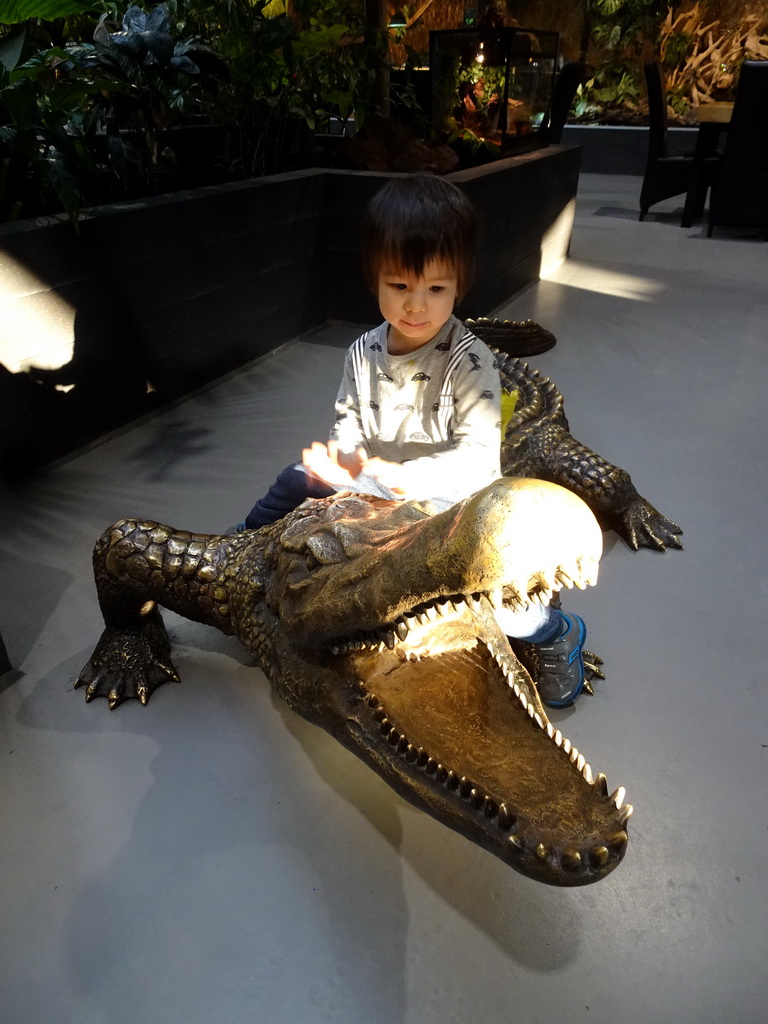 Max sitting on a Crocodile statue at the lower floor of the Reptielenhuis De Aarde zoo