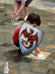 Max with a wooden shield playing with the fountain at the Kasteelplein square, during the Nassaudag