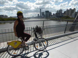Miaomiao on her CityCycle bicycle at the Goodwill Bridge, with a view on skyline of Brisbane with the Infinity Tower, the Victoria Bridge over the Brisbane River and the South Bank Parklands