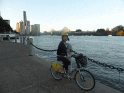 Miaomiao on her CityCycle bicycle at the City Reach Boardwalk, with a view on the skyline of Brisbane with the Soleil Tower and the Story Bridge over the Brisbane River