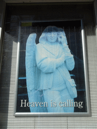 Poster with the statue of an angel with a telephone of St. John`s Cathedral, at the front of the Sint-Jansmuseum at the Torenstraat street