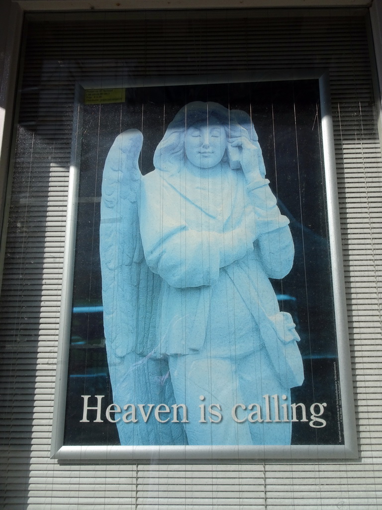 Poster with the statue of an angel with a telephone of St. John`s Cathedral, at the front of the Sint-Jansmuseum at the Torenstraat street