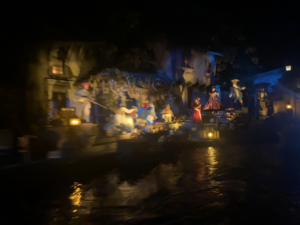 Salesman statues at a market at the Pirates of the Caribbean attraction at Adventureland at Disneyland Park, viewed from our boat, by night