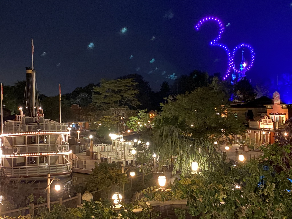 The Thunder Mesa Riverboat Landing attraction and the Silver Sput Steakhouse restaurant at Frontierland and Sleeping Beauty`s Castle at Fantasyland at Disneyland Park, viewed from the staircase to the Phantom Manor attraction at Frontierland, during the Disney D-Light drone show, by night