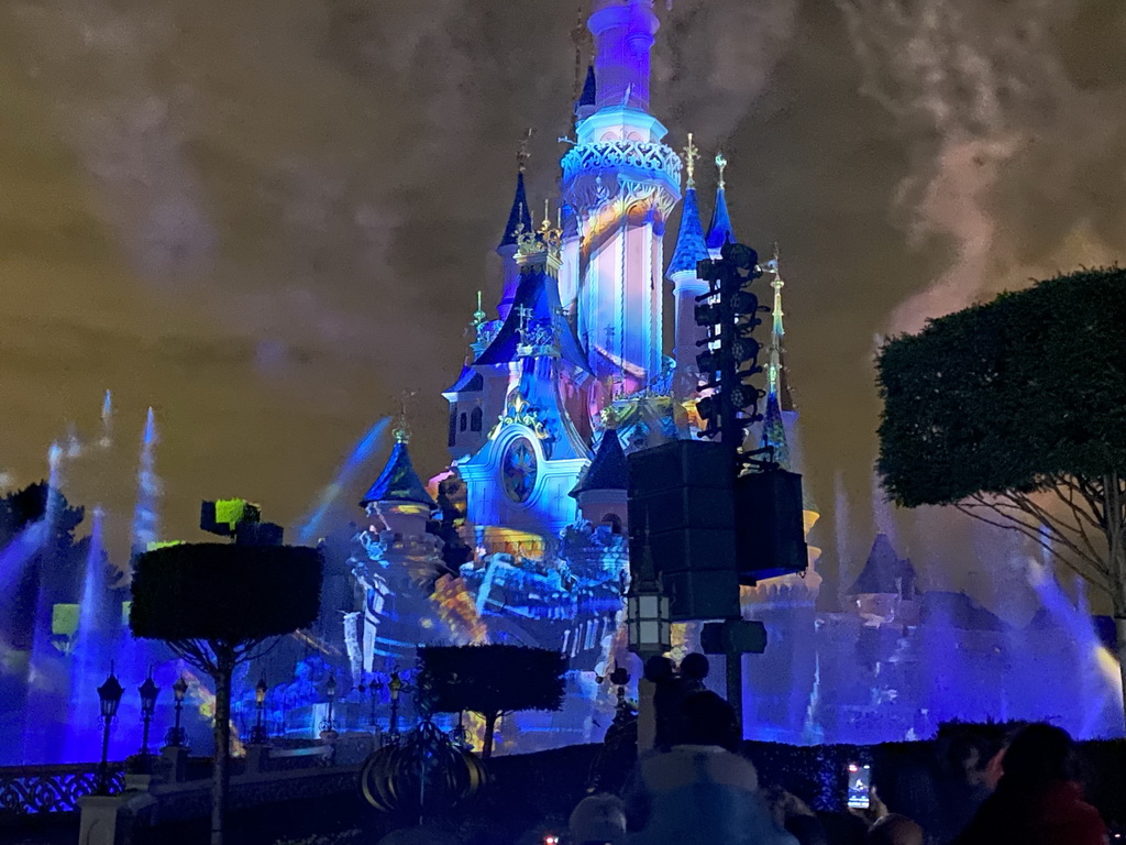 Front of Sleeping Beauty`s Castle at Fantasyland at Disneyland Park, with illuminations and fountains during the Disney Illuminations show, viewed from Central Plaza, by night