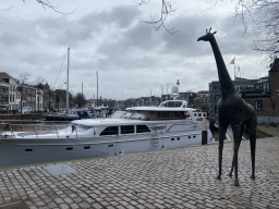 Statue of a Giraffe at the Houttuinen street, with a view on boats at the Nieuwe Haven harbour