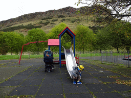 Max on the slide at the playground at Dumbiedykes Road, with a view on Holyrood Park with the Salisbury Crags