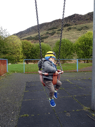 Max on the swing at the playground at Dumbiedykes Road, with a view on Holyrood Park with the Salisbury Crags