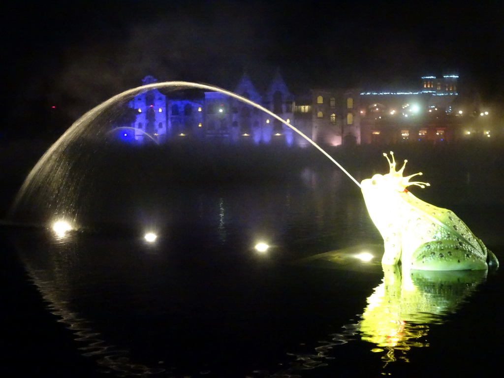 Frog fountain at the Aquanura lake at the Fantasierijk kingdom and the Efteling Theatre at the Anderrijk kingdom, during the water show at the Winter Efteling, by night