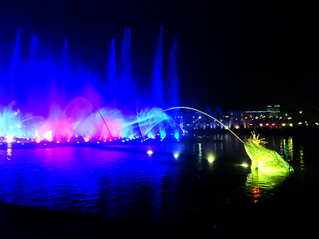 Frog fountain at the Aquanura lake at the Fantasierijk kingdom and the Efteling Theatre at the Anderrijk kingdom, during the water show at the Winter Efteling, by night