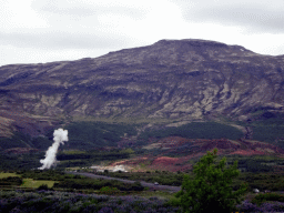 The Biskupstungnabraut road, mountains and the Geysir geothermal area with an erupting Strokkur geyser, viewed from the rental car