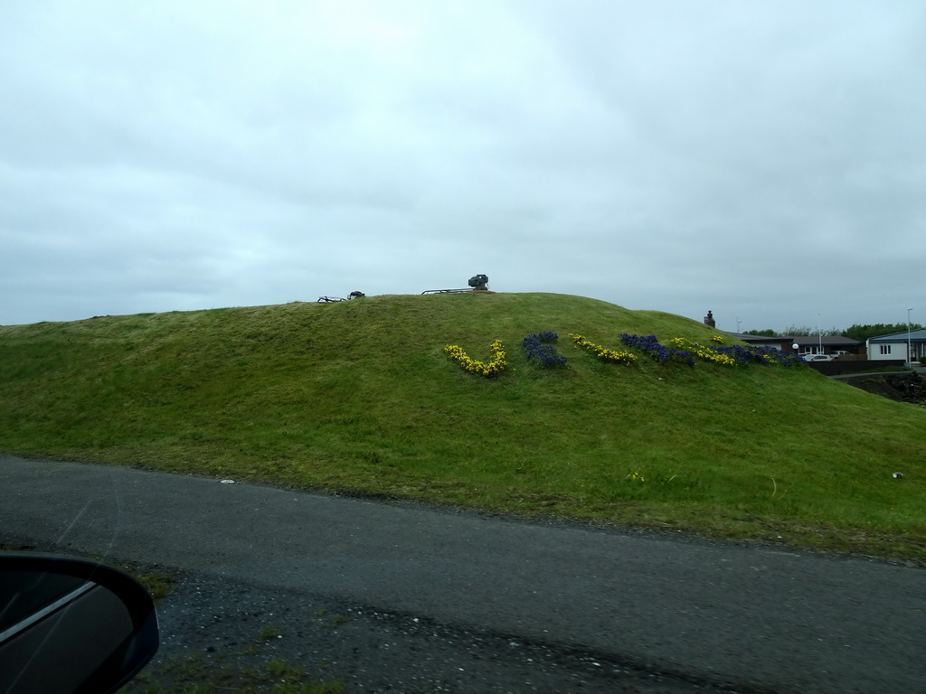 Hill with flowers spelling `Velkominn` at the north side of town, viewed from the rental car on the Grindavíkurvegur road