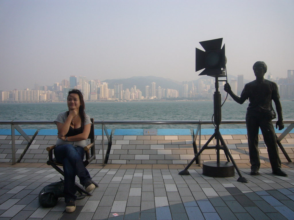 Miaomiao on a movie director`s chair at the Avenue of Stars, with a view on Victoria Harbour and the skyline of Hong Kong