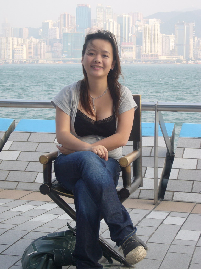 Miaomiao on a movie director`s chair at the Avenue of Stars, with a view on Victoria Harbour and the skyline of Hong Kong