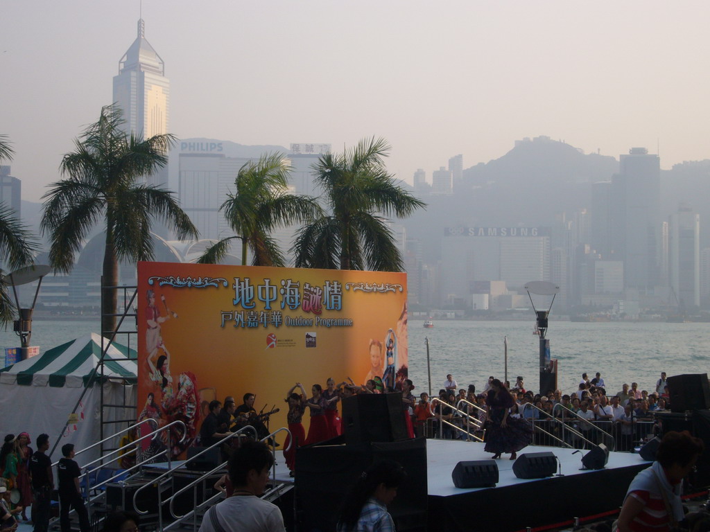 Dancers on a stage in front of the Hong Kong Museum of Art, with a view on Victoria Harbour and the skyline of Hong Kong with the Central Plaza building and the Hong Kong Convention and Exhibition Centre