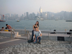 Tim and Miaomiao at the Kowloon Public Pier, with a view on boats in Victoria Harbour and the skyline of Hong Kong with the Central Plaza building and the Hong Kong Convention and Exhibition Centre