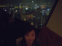 Miaomiao at the restaurant at Victoria Peak, with a view on the skyline of Hong Kong and Kowloon with the Two International Finance Centre, and Victoria Harbour, by night
