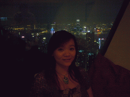 Miaomiao at the restaurant at Victoria Peak, with a view on the skyline of Hong Kong and Kowloon with the Two International Finance Centre, and Victoria Harbour, by night