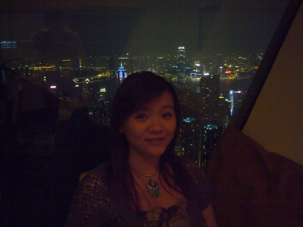 Miaomiao at the restaurant at Victoria Peak, with a view on the skyline of Hong Kong and Kowloon with the Two International Finance Centre, and Victoria Harbour, by night